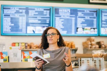 Woman speaking in a cafe with menu boards behind her.