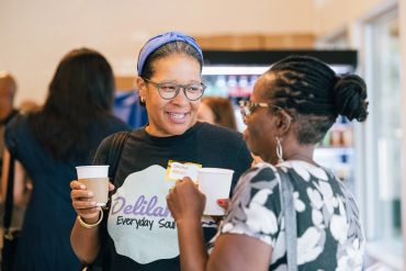 Two women chat and smile while holding coffee cups.