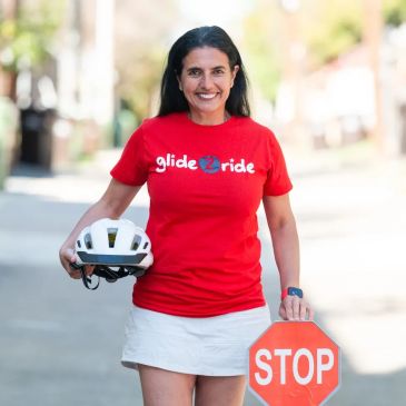 Woman in red shirt holding helmet and stop sign.
