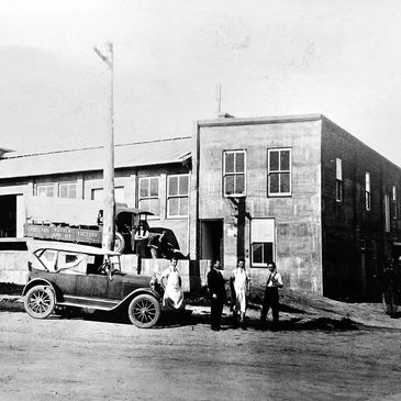 Black and white photo of vintage cars and men outside an early 20th-century building.