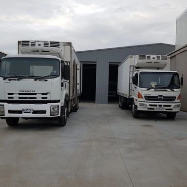 Two refrigerated trucks parked outside a warehouse.