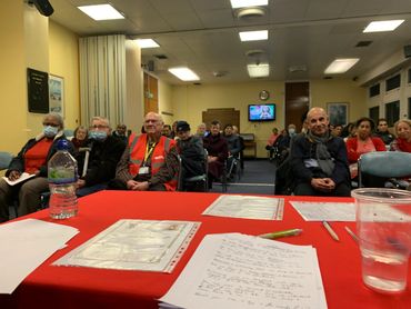 Audience attentively listens during a community meeting in a modest room.