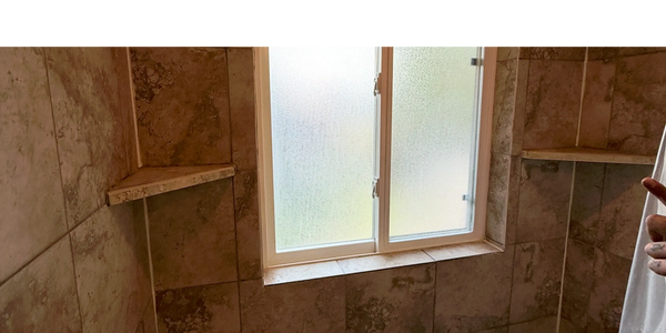 A tiled bathroom shower area with a frosted window and corner shelves.