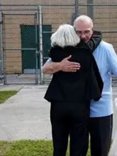 An emotional hug between two people outside a fenced area.