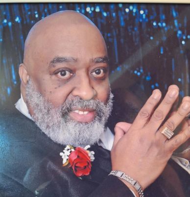Smiling elderly man with a white beard and a red rose on his lapel.