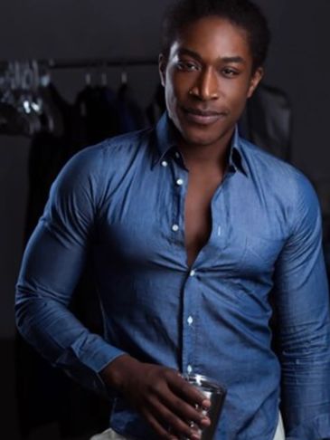 Confident man in a blue shirt holding a drink and smiling.