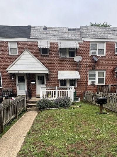 Brick townhouse with white awnings and fenced yard under gray sky.