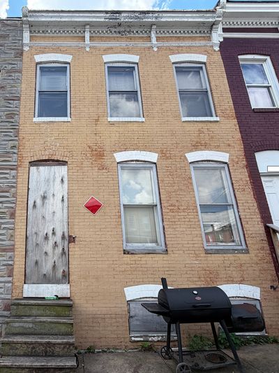 Old brick row house with boarded-up door and windows, and a grill outside.