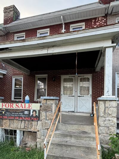 Front porch of a brick house with a for sale sign.