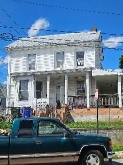 Old white house with a porch and a green pickup truck parked in front.