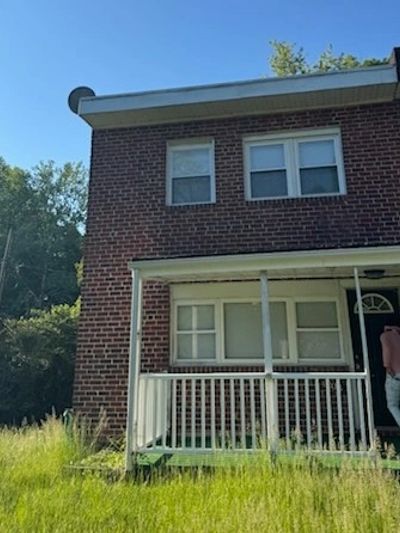 Two-story brick house with a small porch and overgrown lawn.