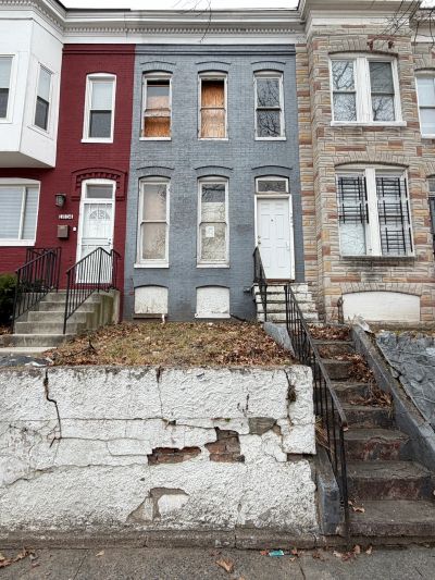 Abandoned row house with boarded windows and peeling paint.