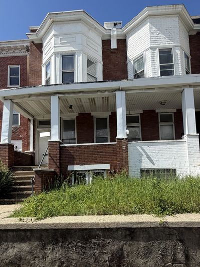 Two attached brick row houses with front porches and overgrown grass.