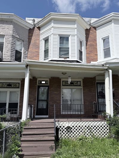 Brick row house with front porch and stairs leading to a grassy yard.