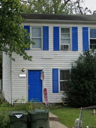 White two-story house with blue door and shutters, surrounded by greenery.