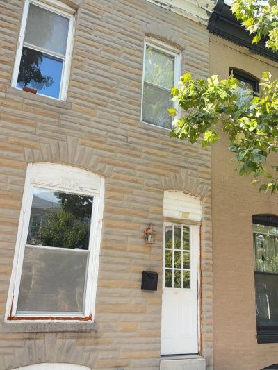 Front view of a beige brick townhouse with a white door and windows.