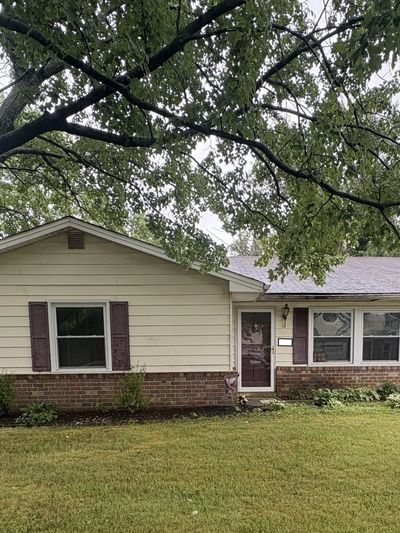 Single-story house with beige siding and a large tree in front yard.