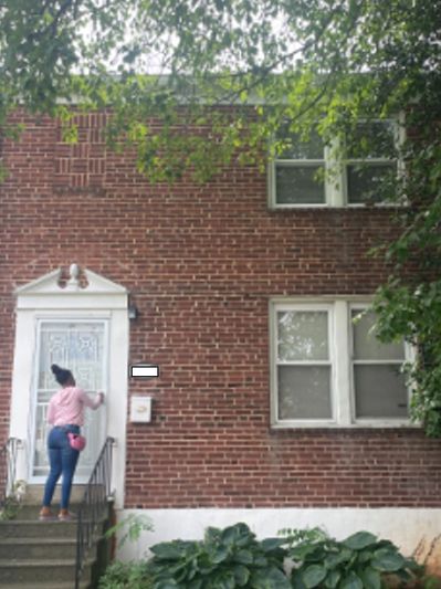 Person knocking on a brick house door with white trim and steps.