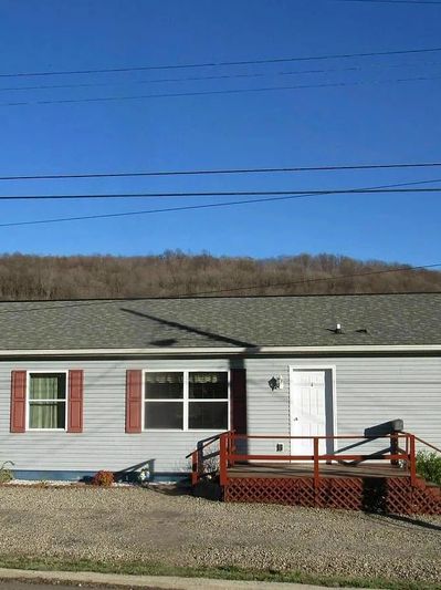 Single-story house with gray siding and red shutters under a clear sky.