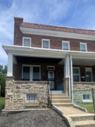Brick house with stone foundation and front porch under blue sky.