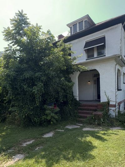 Altes, weißes Haus mit überwucherter Vegetation davor.