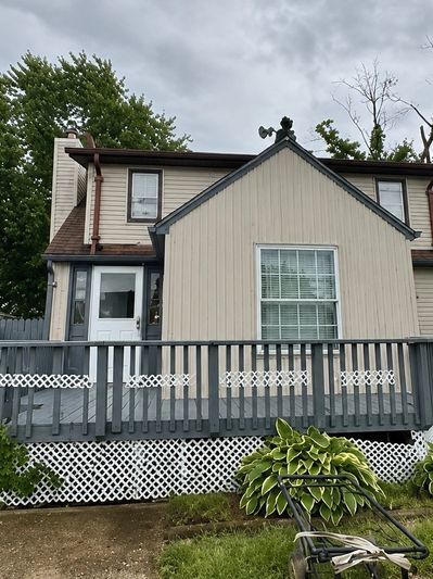 A two-story house with beige siding and a wooden deck under a cloudy sky.