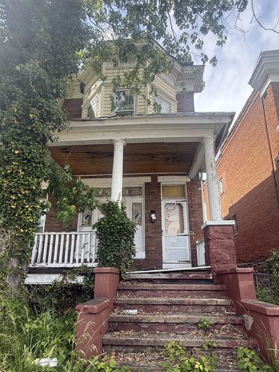 Old, rundown house with peeling paint and overgrown plants.