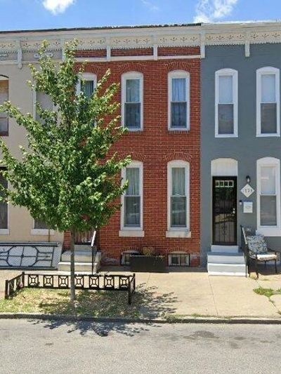 Row of three townhouses with a small tree and benches in front.