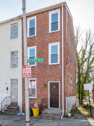 Narrow three-story brick house on a corner lot with street signs and steps.