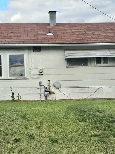 Backyard view of a modest house with a green lawn and windows.