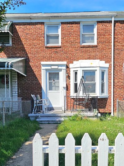 Brick townhouse with white door and windows, small front porch, and white picket fence.