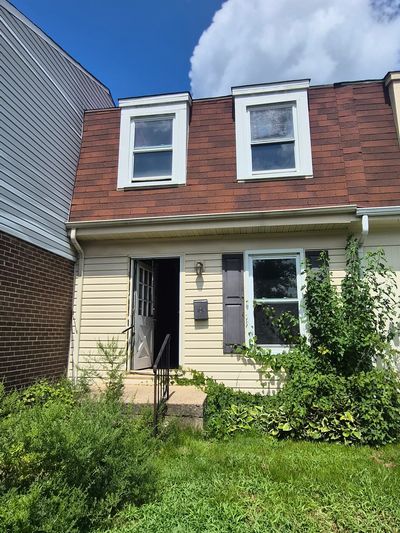 Two-story house with overgrown front yard and partly open door.