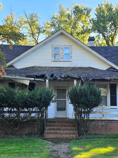 Old house with worn roof and overgrown bushes.