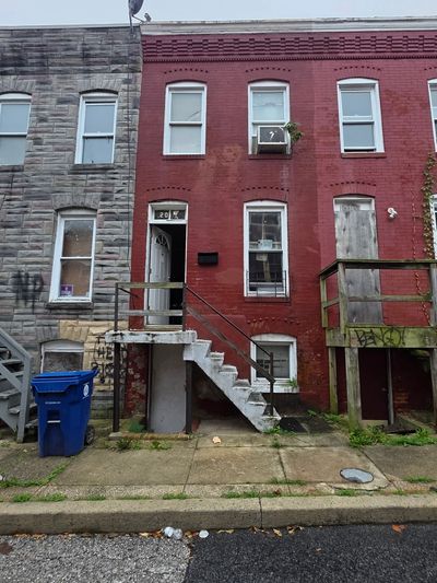 Old brick row house with stairs and boarded window.