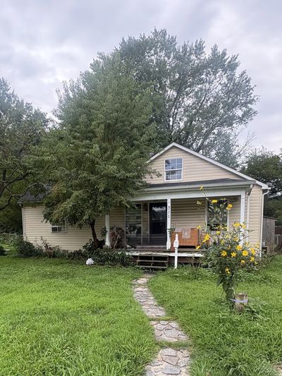 Small beige house with front porch and garden path.