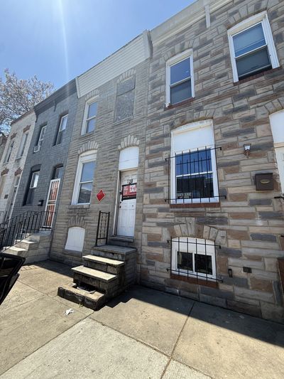 Row of brick townhouses with a 'For Sale' sign on one door under a sunny sky.