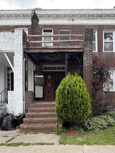 Old brick row house with a small porch and green shrub in front.