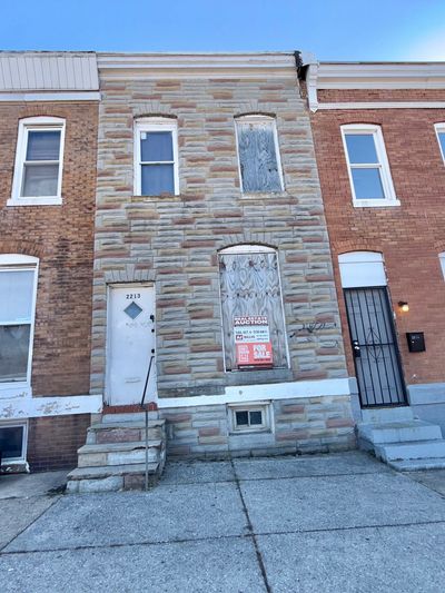 Old row house with boarded windows and an auction sign.