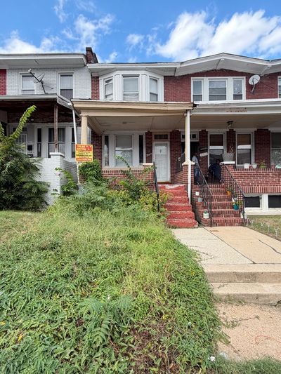 Two adjacent brick row houses with porches and overgrown lawns.