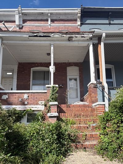 Old brick house with overgrown plants and worn stairs.