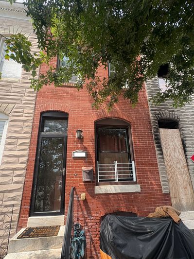 A brick townhouse with a black door and window under tree shade.