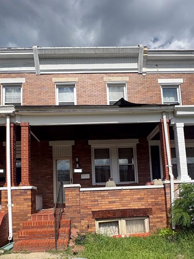 Brick townhouse with a covered front porch under cloudy sky.