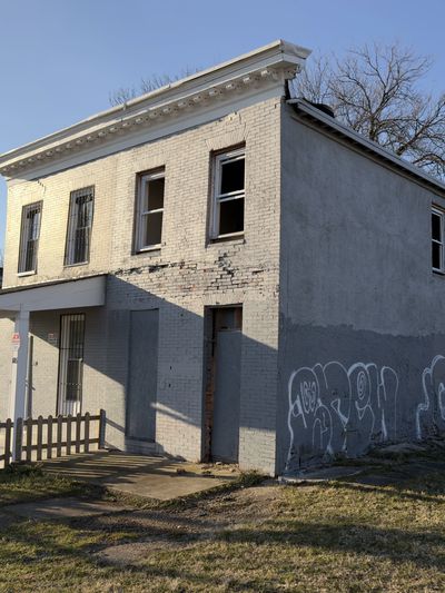 Old two-story house with cracked paint and graffiti on side wall.