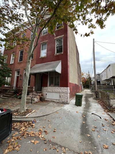 Three-story brick row house with a tree and fallen leaves in front.