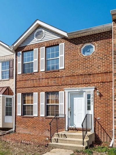 Two-story brick townhouse with white shutters and door.