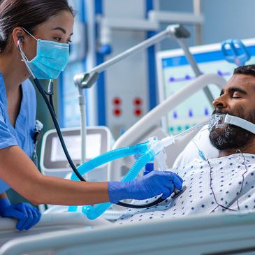 Two healthcare staff in protective suits attend to a patient in the ICU environment.