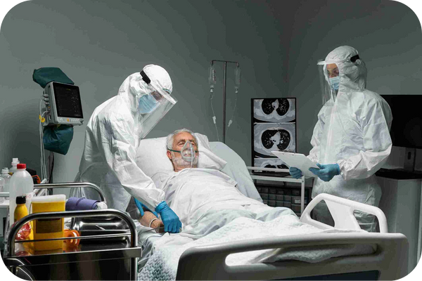 Two healthcare staff in protective suits attend to a patient in the ICU environment.
