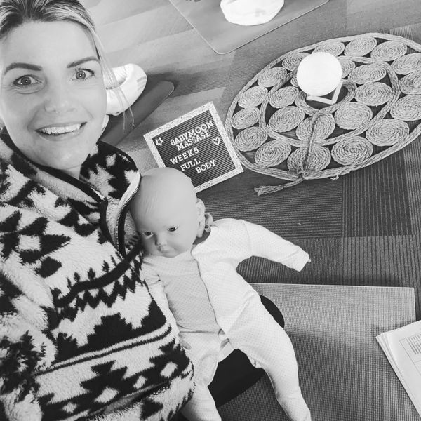 Woman smiling with a baby doll and a sign about babymoon massage week 5 full body.