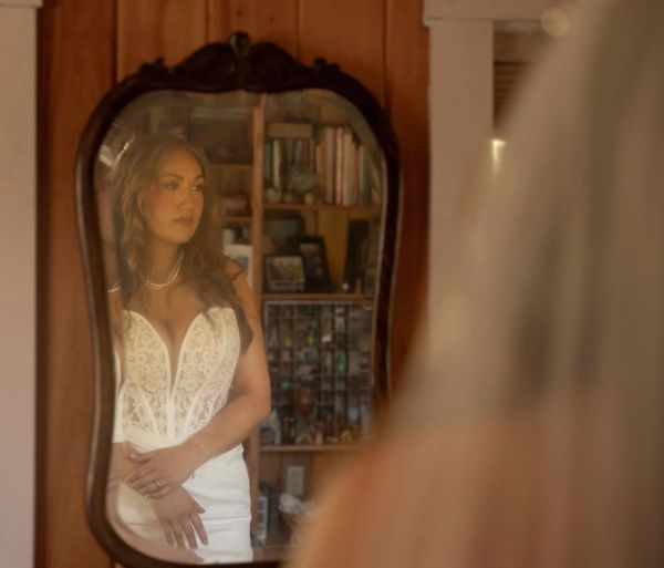 Bride in white dress looking at herself in mirror.