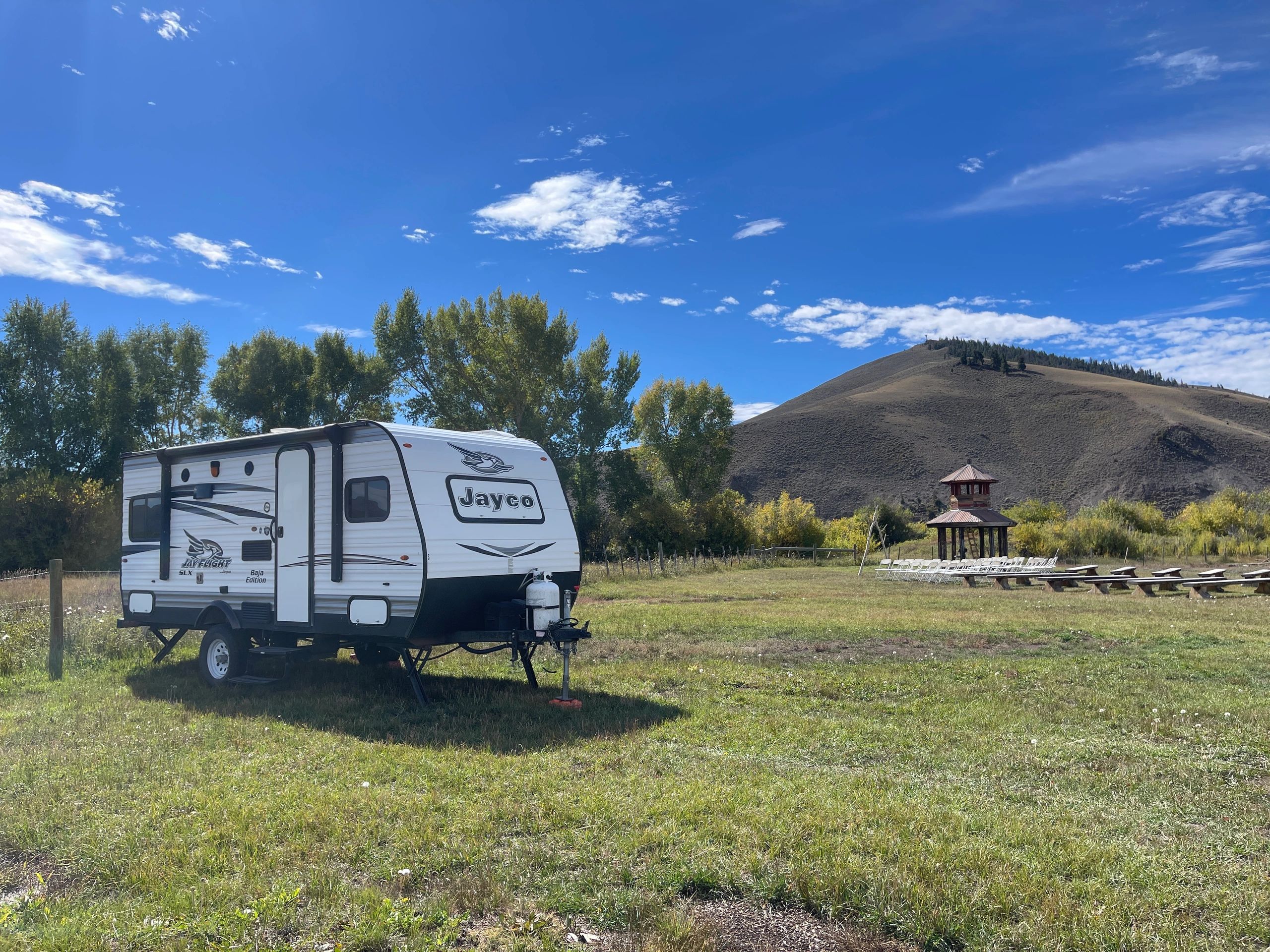 A Jayco RV in a grassy campsite with hills and blue sky.